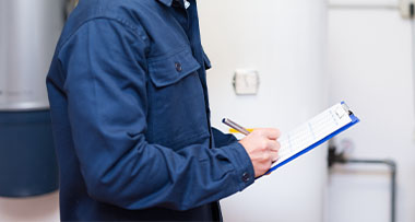 a man in blue overalls performing a gas safe inspection and writing notes on a blue clipboard