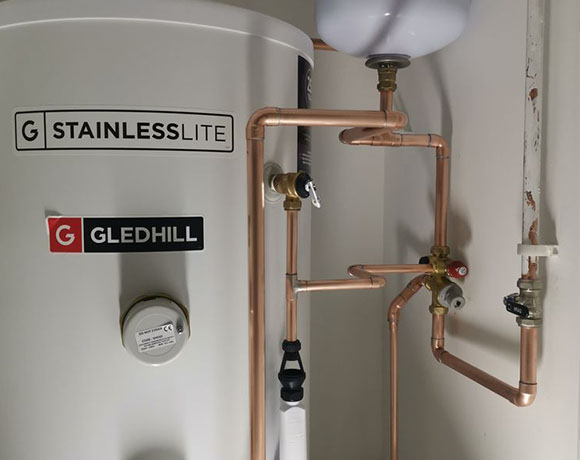 a boiler and heating cylinder installed in a cupboard with copper water pipes