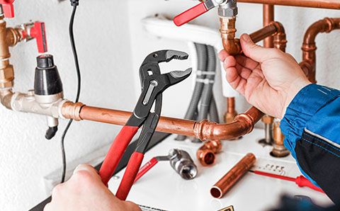 a person using an adjustable wrench to install copper piping for a heating and plumbing system