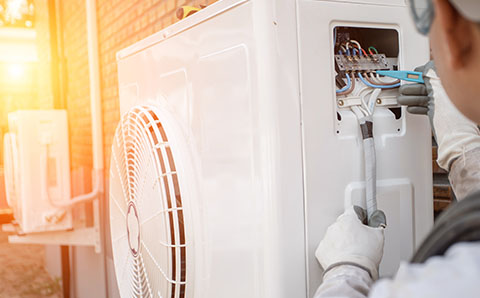 a man installing heat air pump units outside of a brick property